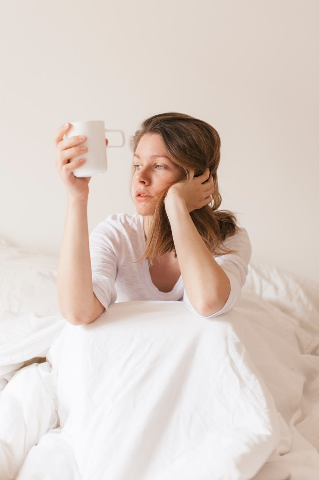 Mujer sentada en la cama, sosteniendo una bebida caliente, enferma de Covid