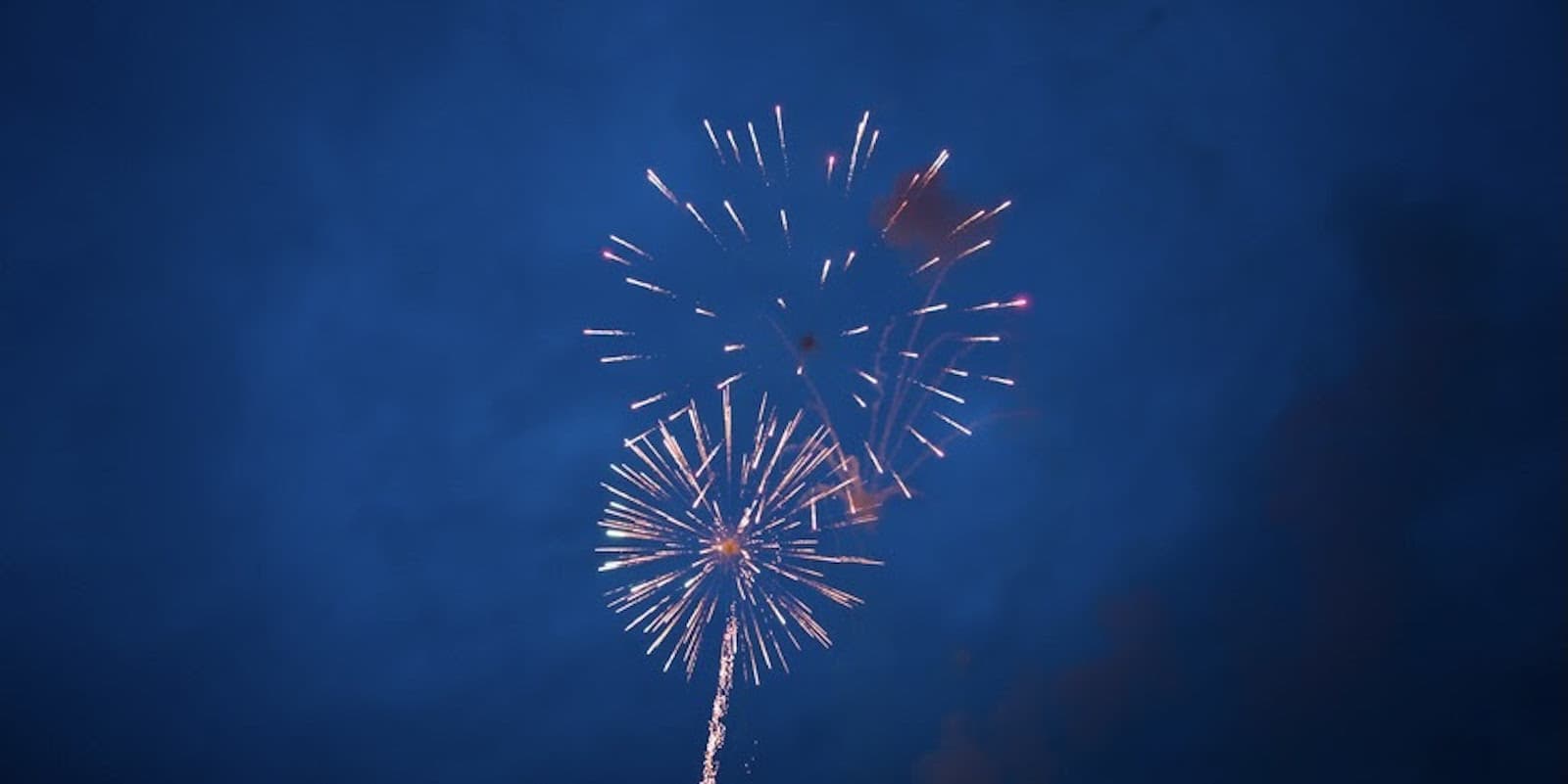 Una fotografía de un cielo azul oscuro con dos fuegos artificiales en medio de una explosión en el centro.