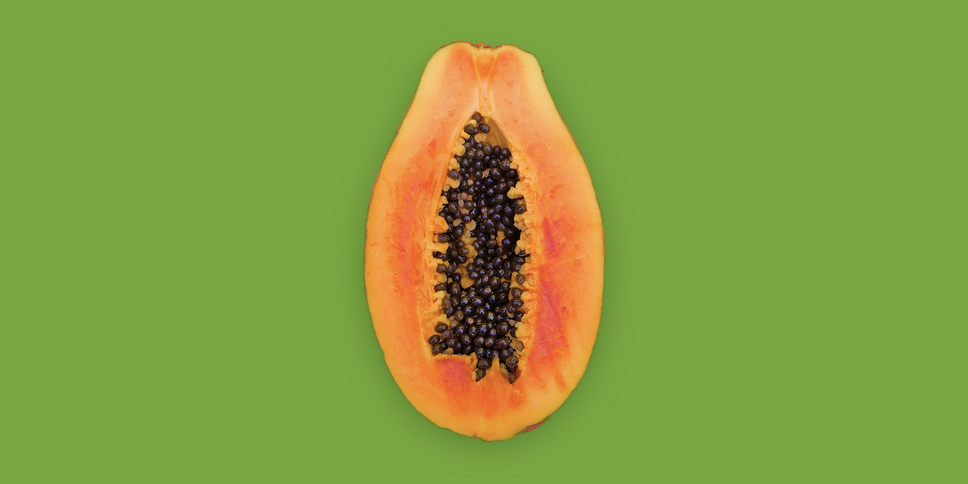 Una papaya anaranjada cortada por la mitad descansa sobre un fondo verde hierba