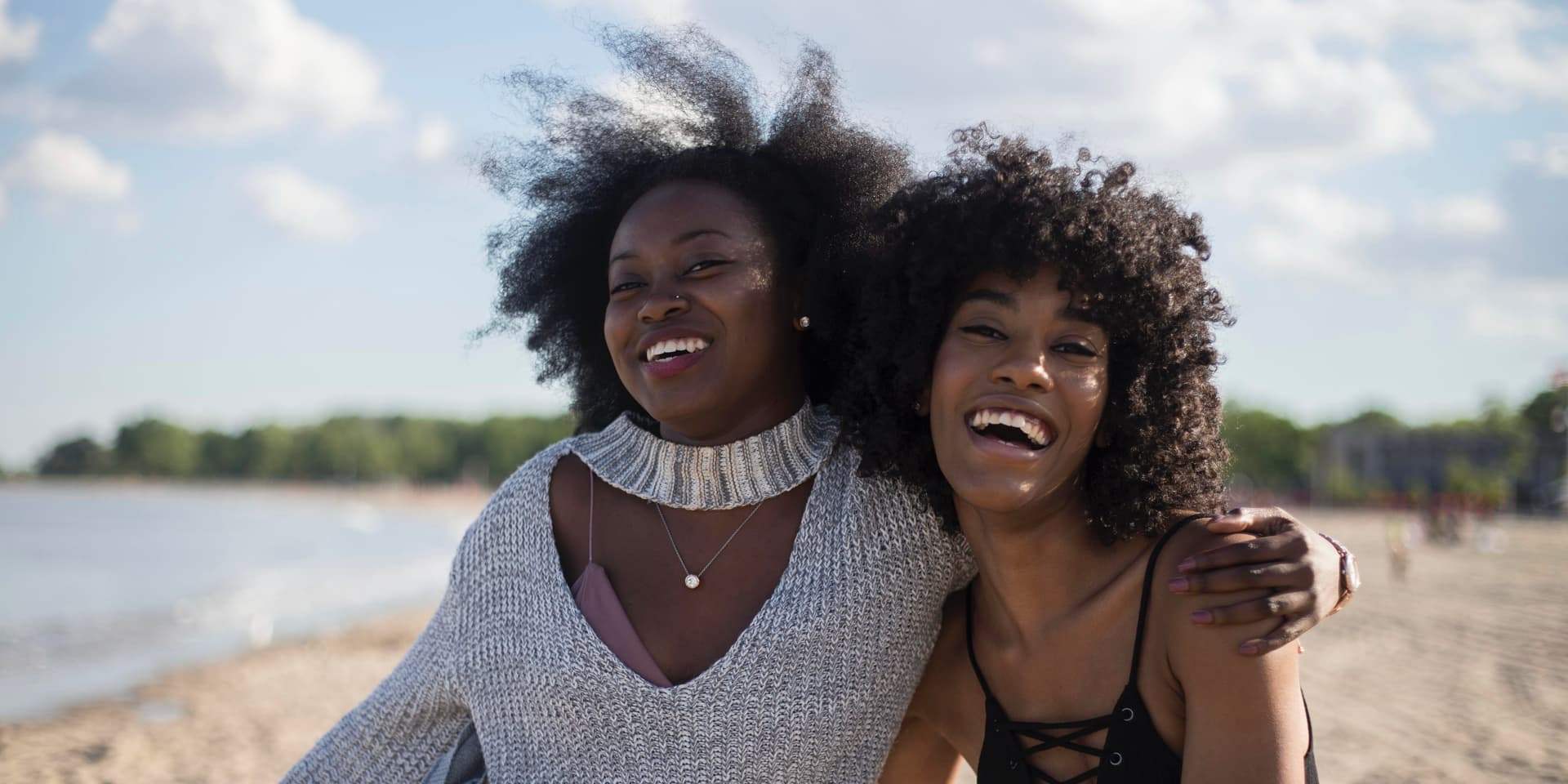 Dos jóvenes negras con afros abrazándose y sonriendo en la playa en un día soleado