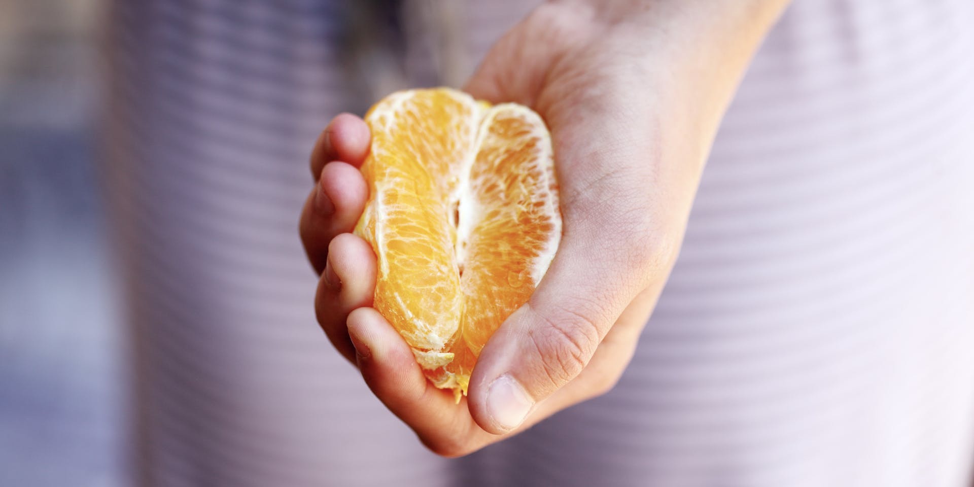 La mano de una mujer blanca, sosteniendo media naranja