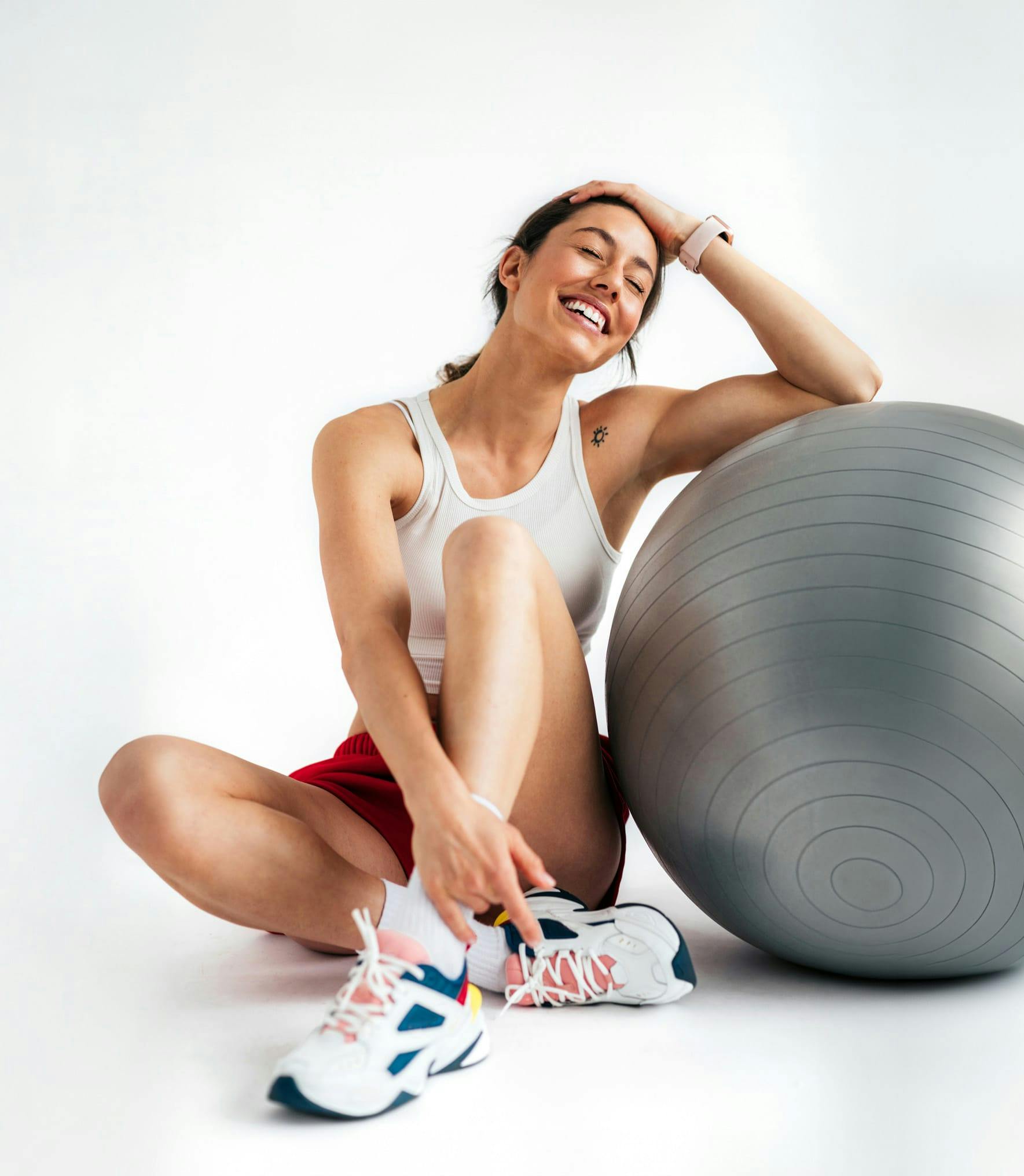 Una mujer con ropa deportiva sentada y sonriendo apoyada en una pelota de entrenamiento