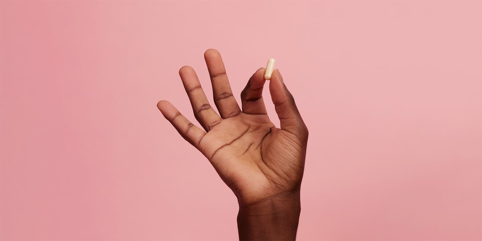 Una mano femenina oscura que sostiene una pastilla apretada entre el índice y el pulgar
