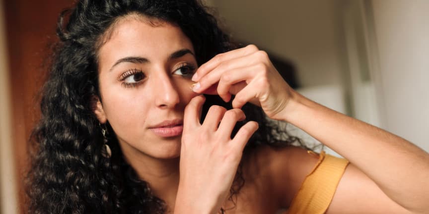 Mujer joven de piel aceitunada, que se aplica aceite esencial para hidratar su rostro como parte de su rutina de belleza.