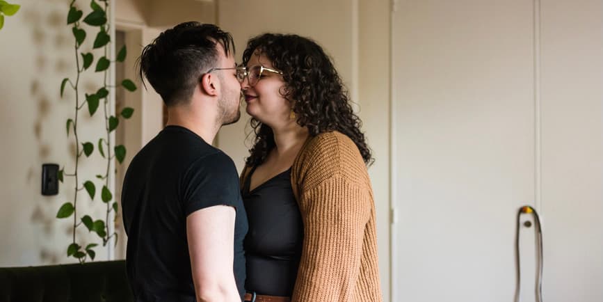 Retrato de linda pareja con curvas besándose dulcemente en casa. Se ven reales y auténticos.