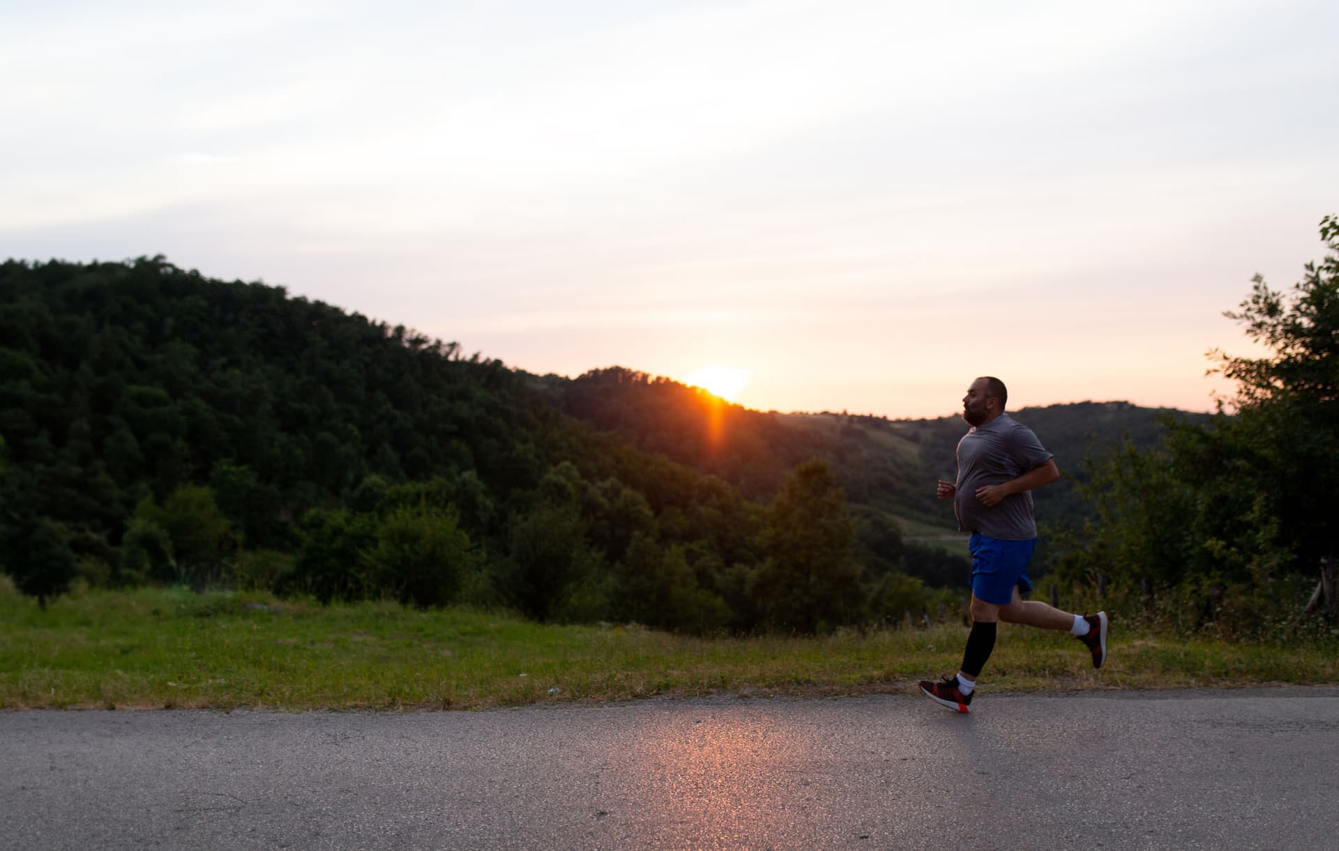 Hombre corriendo por una carretera desnuda con una ladera y una puesta de sol de fondo