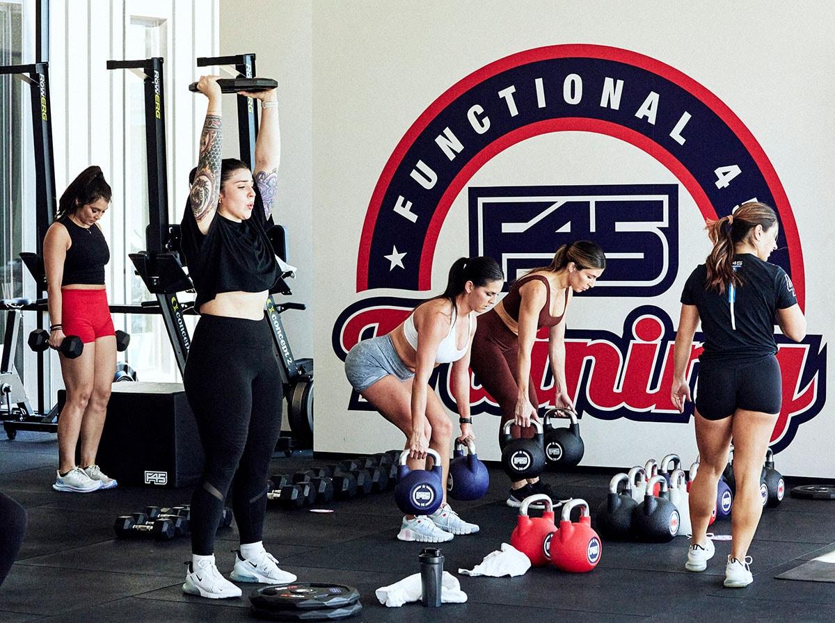 Una clase de entrenamiento de F45 en la que un entrenador ayuda a las personas a levantar pesas