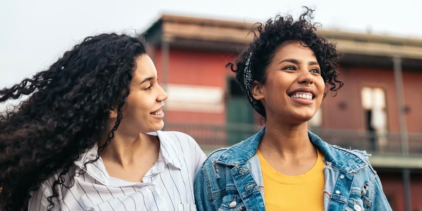 Jóvenes latinas de cabello rizado paseando por la ciudad sonriendo.