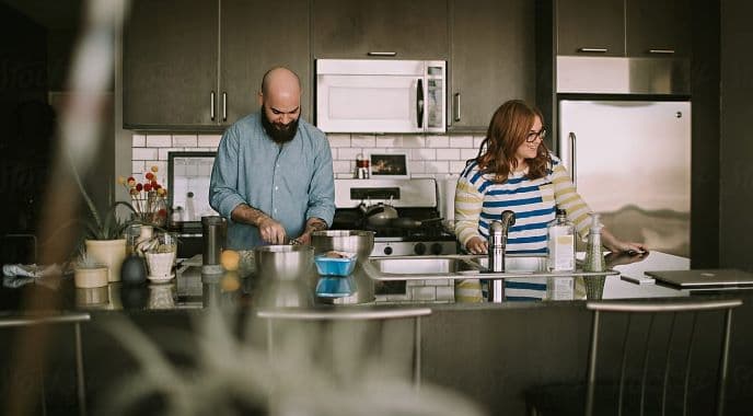 Una pareja prepara la comida en una cocina moderna con electrodomésticos de acero inoxidable y luz natural.