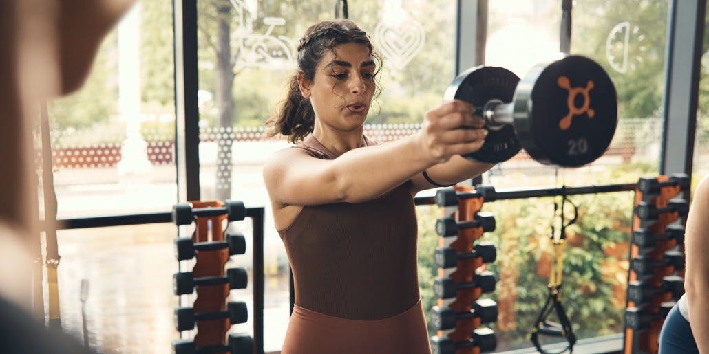 Una mujer joven se concentra mientras levanta un peso pesado durante una clase de Orangtheory Fitness.