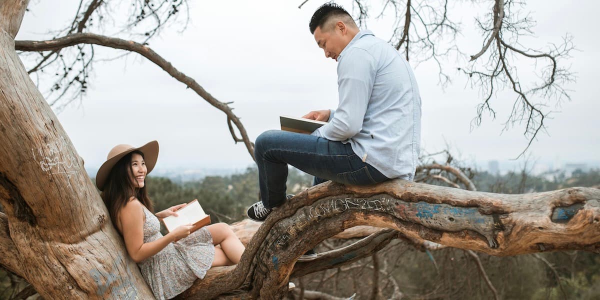 Una pareja asiática joven y atractiva se sienta en un árbol, leyendo libros y sonriendo.