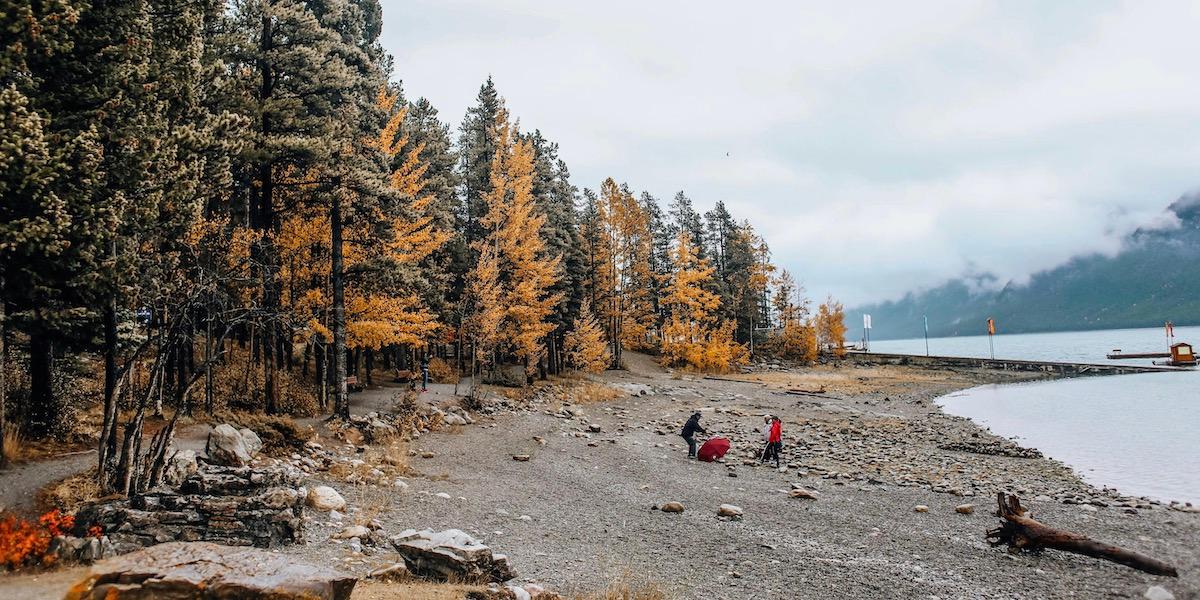 Imagen lejana de dos personas en la orilla de un lago en otoño.