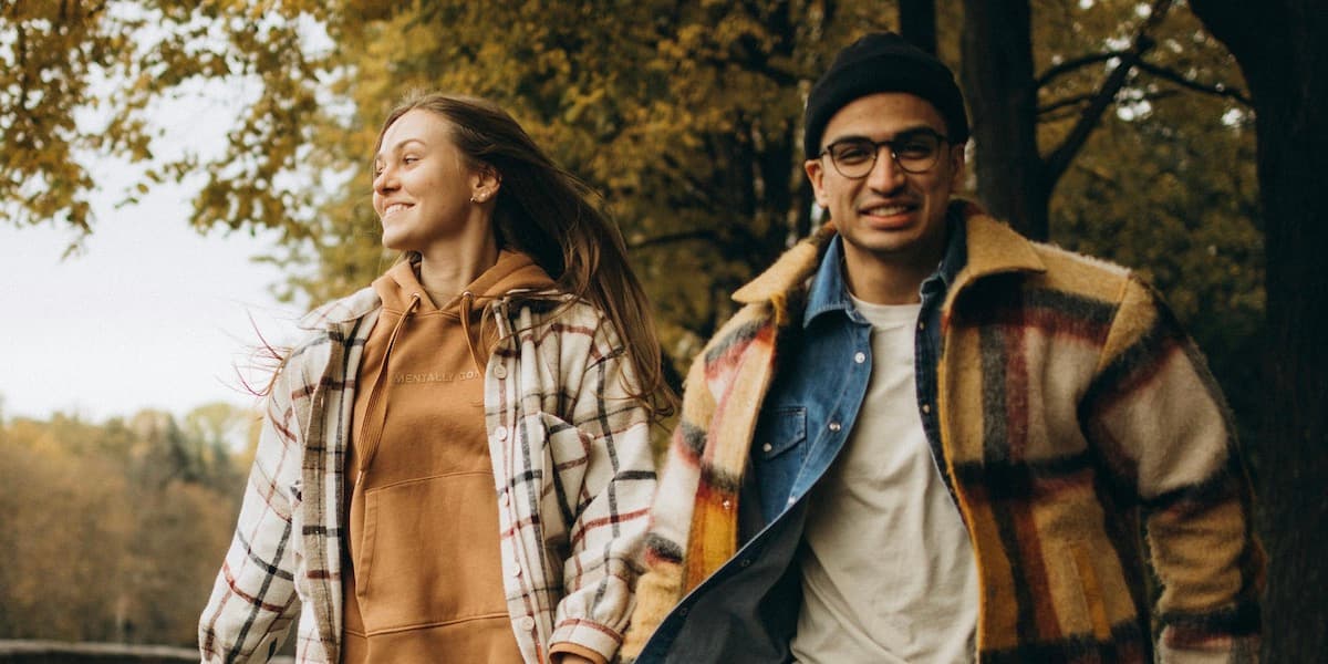 A young couple in casual clothing runs through a city park in the fall.