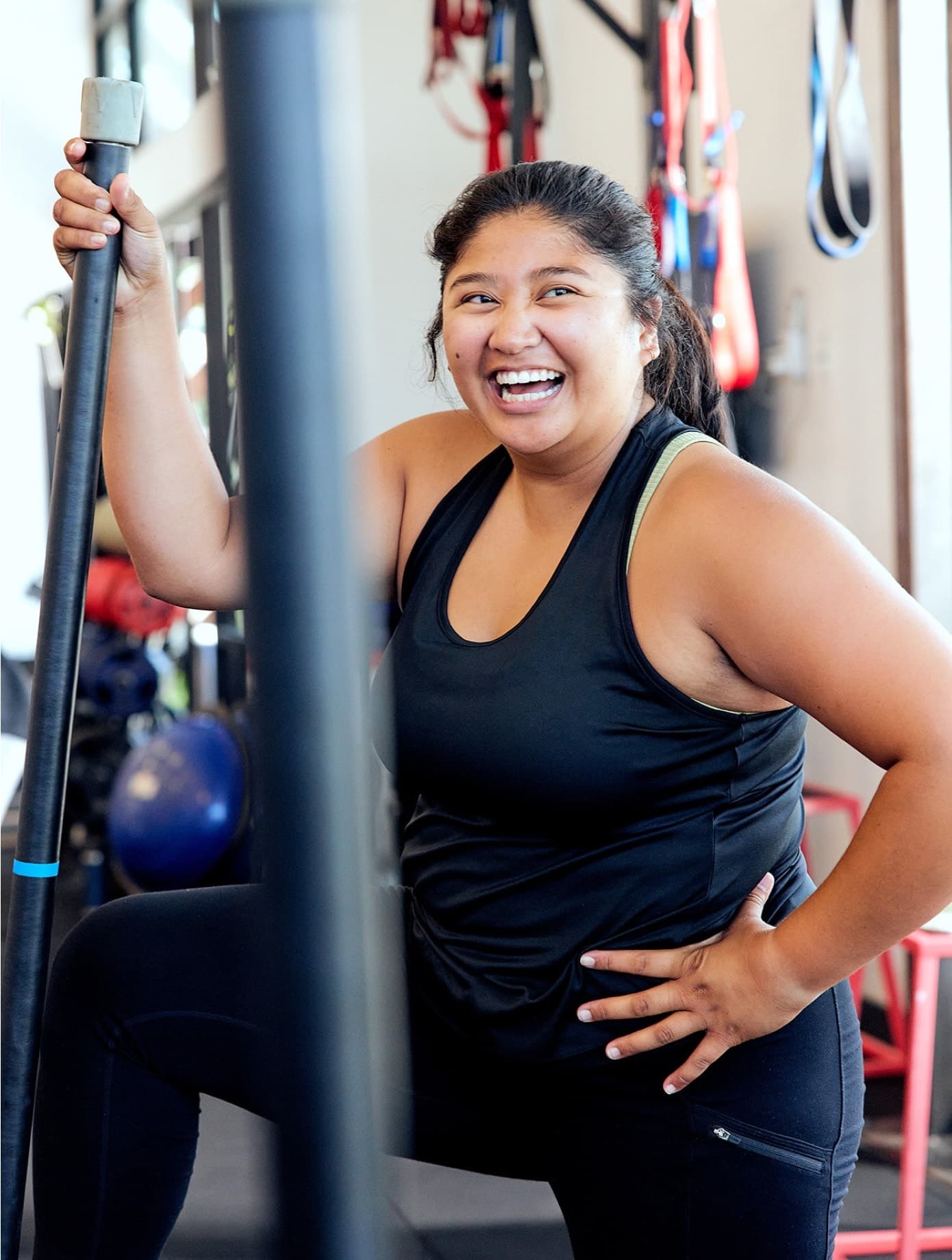 Mujer sonriente vestida con ropa deportiva negra en el gimnasio F45 Training, sujetando la barra con una pierna en el banco